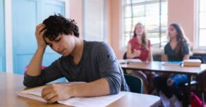 A student appears stressed while studying in a classroom setting, highlighting educational challenges.