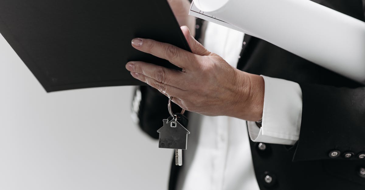 Close-up of a business professional holding a house key and architectural plans, symbolizing real estate.