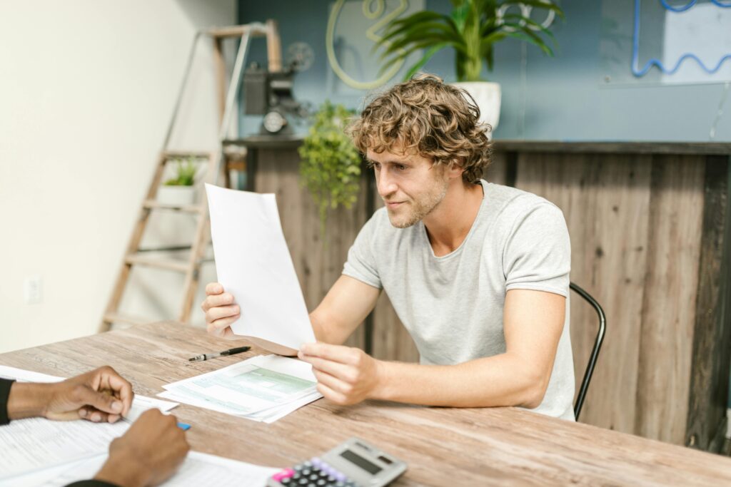 A man with curly hair evaluates documents at a desk, highlighting focused work in a professional setting.
