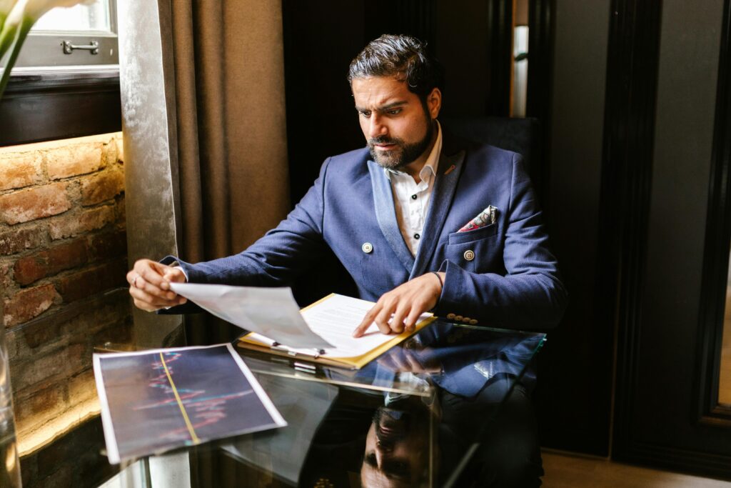 Businessman in blue blazer reviewing financial documents at a glass table.
