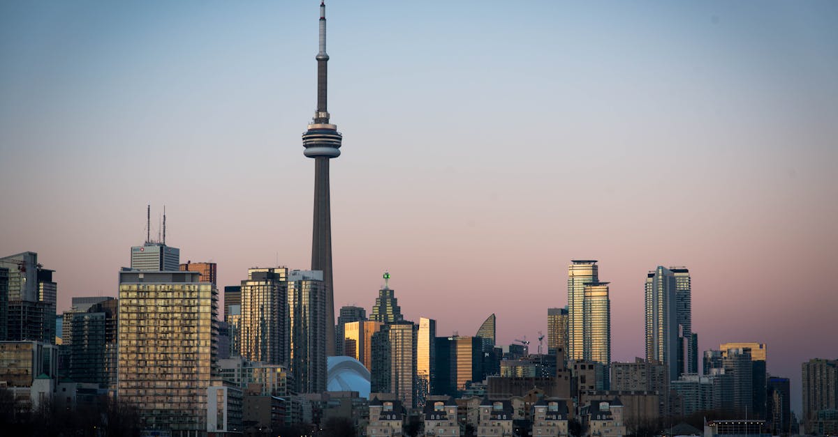 View of Toronto skyline featuring the CN Tower during dusk with cityscape reflections on Lake Ontario.